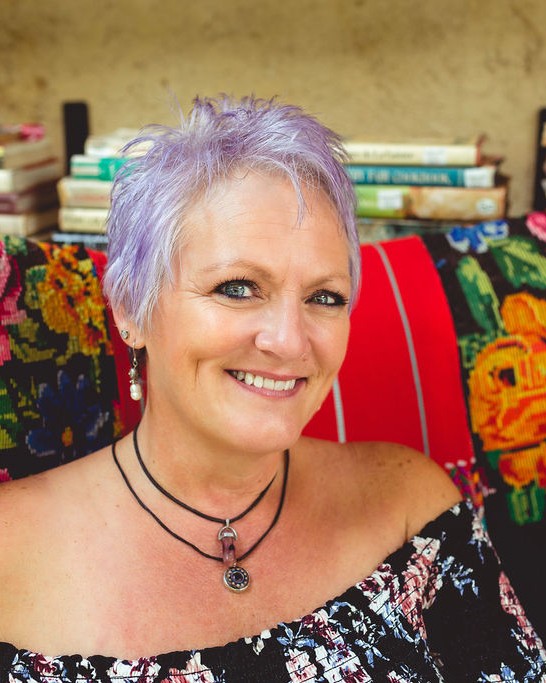 Ronda Taylor smiling, seated in a colorful embroidered chair in Antigua, Guatemala